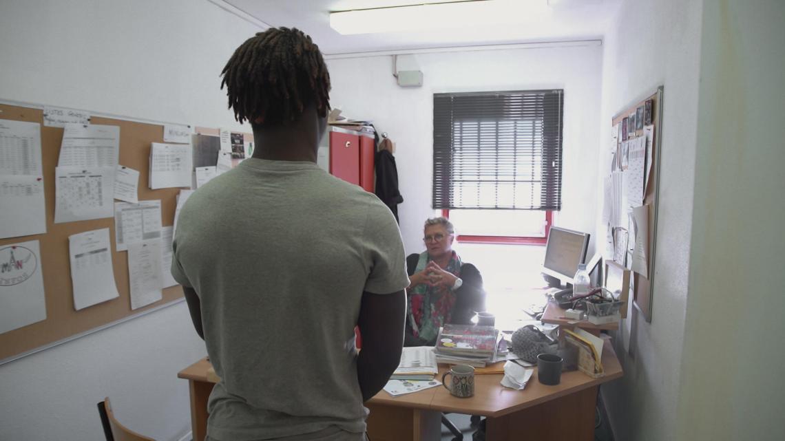 Un détenu se tient debout devant le bureau d'un professeur